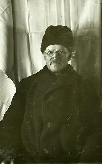 Gammalt svartvitt fotografi föreställande man med vinterjacka och mössa. Mannen har glasögon och mustach.